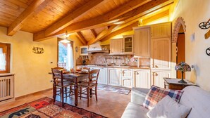 Een gezellige keuken met houten balken, een eethoek met een tafel en stoelen, en een bank met een decoratief plaid.
