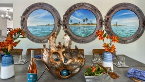 A dining table with three porthole windows, a decorative shell centerpiece, and a bottle of Matua wine. - Luxury Boating Paradise+Pool+Sailing Kayaks (Marathon)