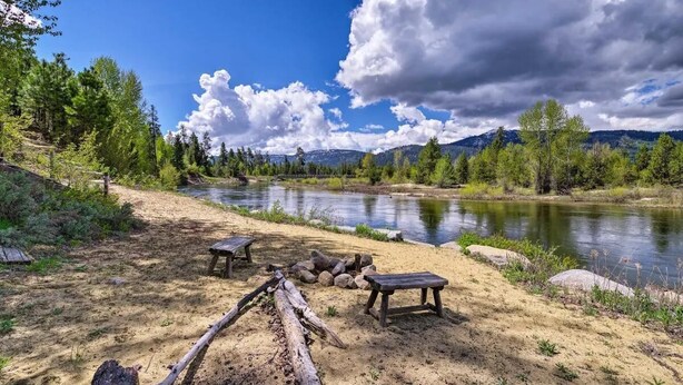 Ein Campingplatz am Flussufer mit Picknicktischen und einer Feuerstelle.