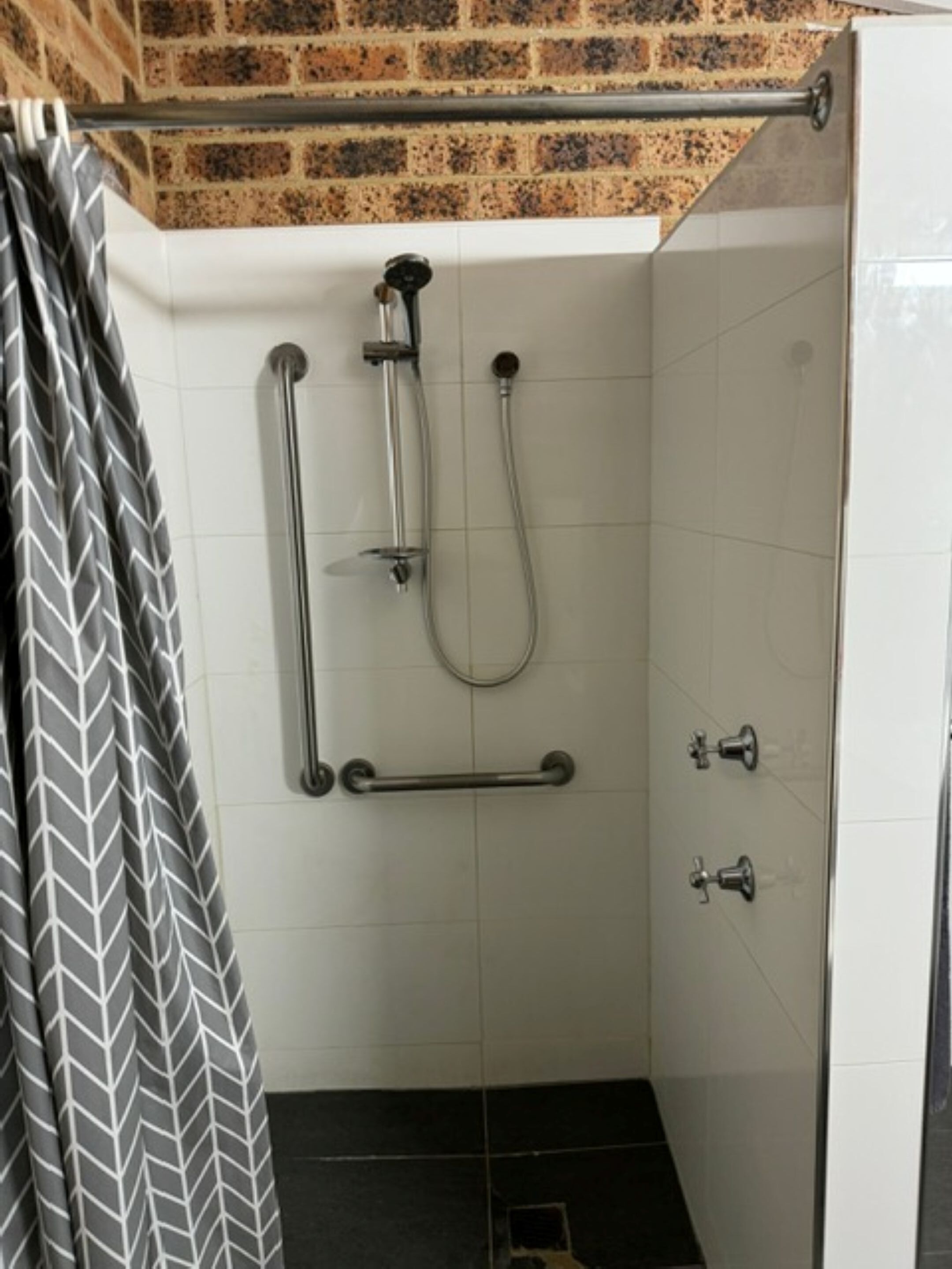 A shower with a handheld showerhead, a handheld shower attachment, and a grab bar.