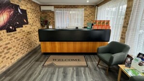 A reception area with a wooden reception desk, two armchairs, a welcome mat, and a wall with a space-themed artwork. - Clock Tower Motor Inn (Coonabarabran)