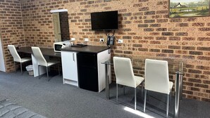 A room with a brick wall, a flat-screen TV mounted above a desk, and a painting of a rural scene. - Clock Tower Motor Inn (Coonabarabran)