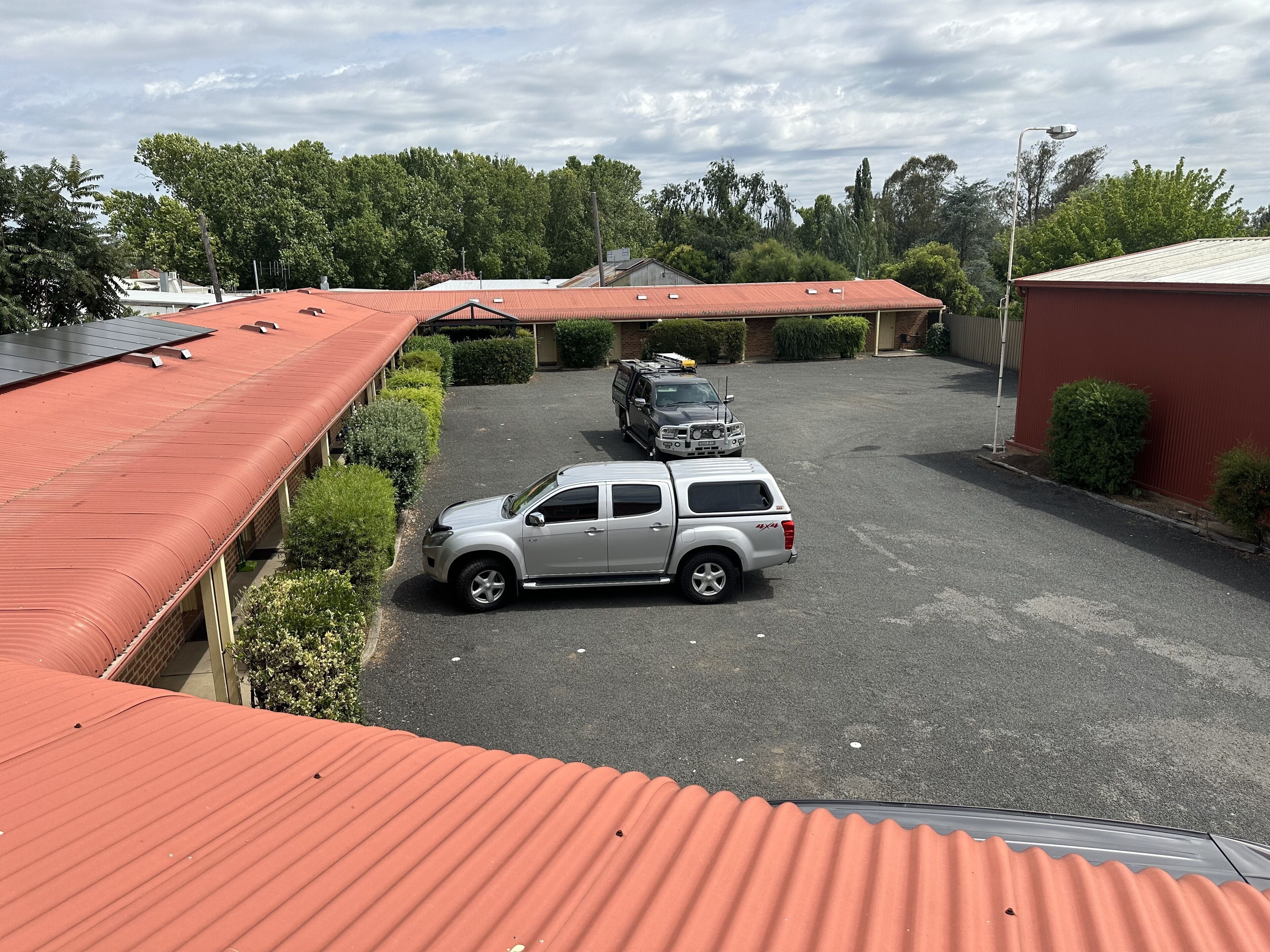 Un estacionamiento con dos SUV, un edificio de techo rojo y vegetación circundante.