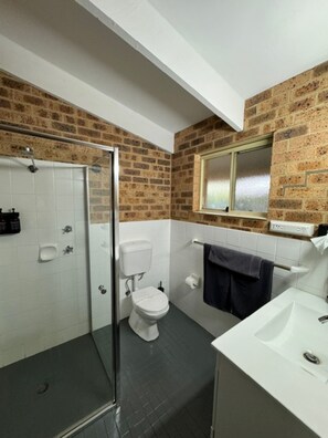 A bathroom with a shower, toilet, and sink, featuring brick walls and a window.