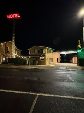 A motel with a prominent red neon sign, a brick building, and a covered parking area.