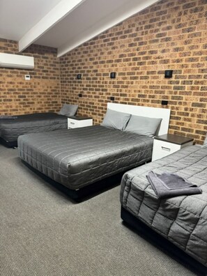 A hotel room with three beds, a brick wall, and a white ceiling.