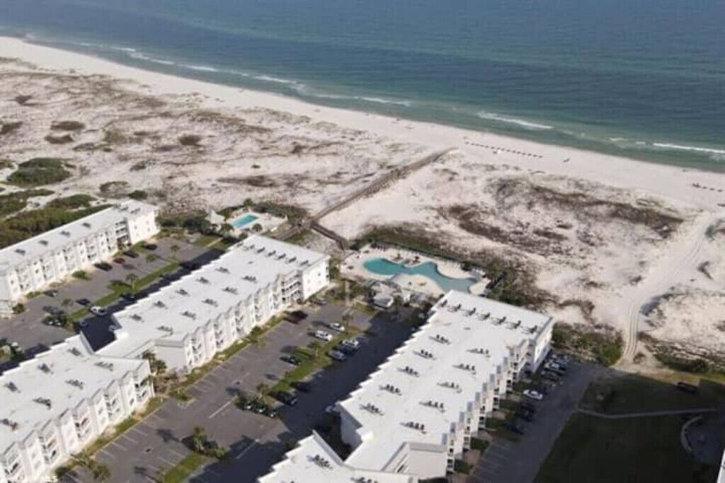 A coastal hotel with multiple buildings, a parking lot, and a beach.