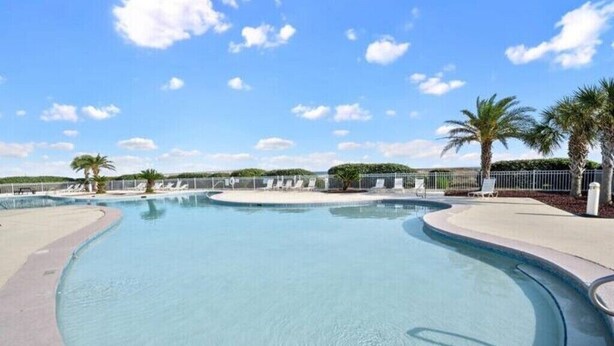 A large, curved swimming pool with a clear blue sky and palm trees in the background. - Brower's Plantation Palace

 (Gulf Shores)