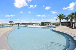 Une grande piscine à débordement aux formes arrondies, avec un ciel bleu dégagé et des palmiers en arrière-plan.