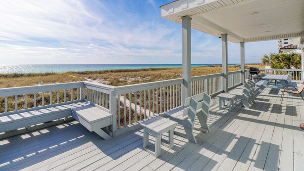 A covered deck with white railings and benches overlooking a beach.