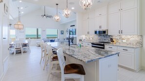 A spacious kitchen with white cabinetry, a granite countertop, and a large island with bar stools.