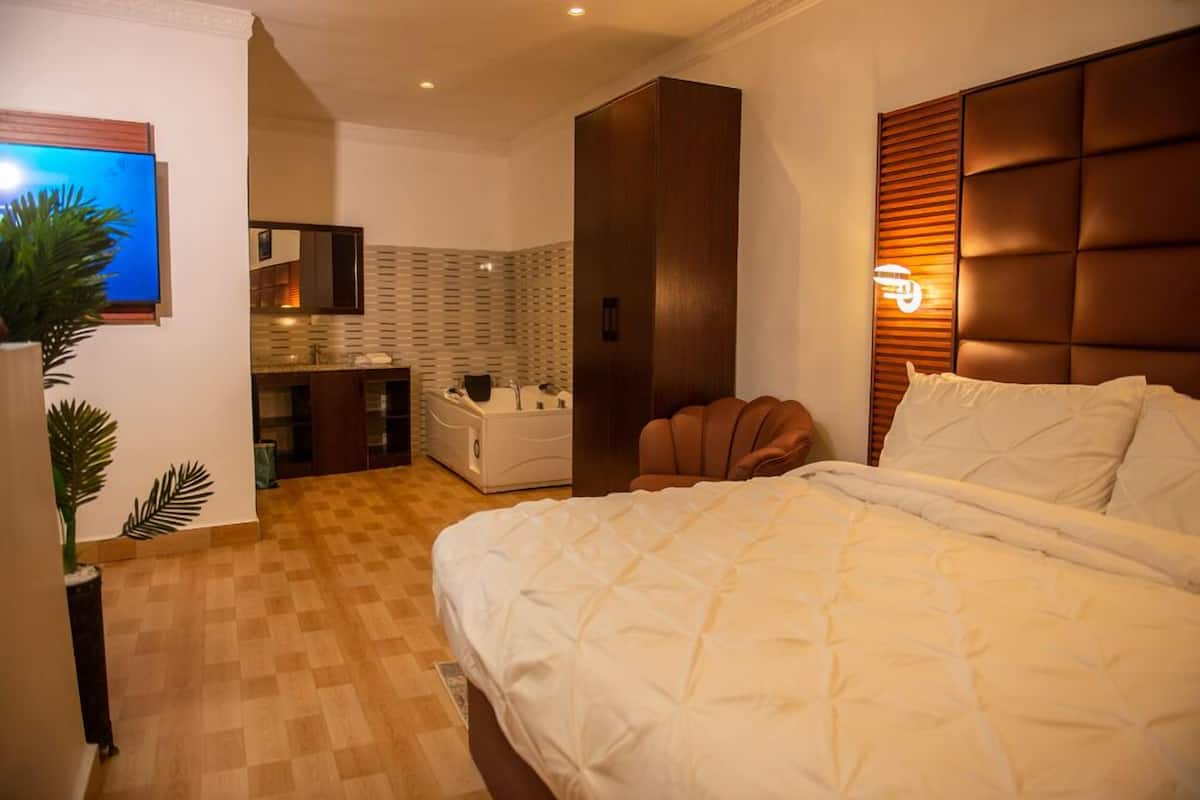 Een moderne hotelkamer met een groot bed, een houten hoofdbord, een inbouw wastafel en een klein zithoekje.