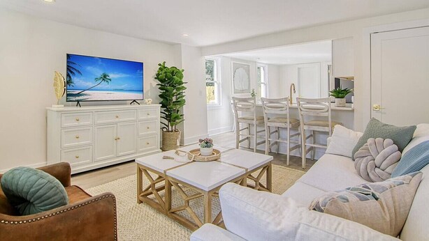 A living room with a white sofa, a coffee table, a TV, and a dining area with chairs and a table. - Renovated - Old Village - Close to Beach/Downtown (Mount Pleasant)