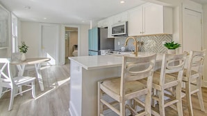 A modern kitchen with white cabinetry, a central island with bar stools, and a microwave above the island. - Renovated - Old Village - Close to Beach/Downtown (Mount Pleasant)