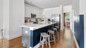 Una cocina moderna con armarios blancos, electrodomésticos de acero inoxidable y una isla central con taburetes de bar.
