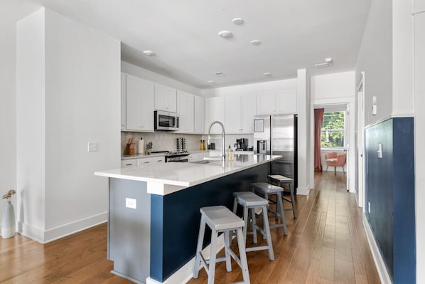 Una cocina moderna con armarios blancos, electrodomésticos de acero inoxidable y una isla central con taburetes de bar.