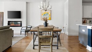 Una sala moderna con chimenea, un comedor con mesa y sillas de madera, una cocina con armarios blancos y un televisor montado en la pared.
