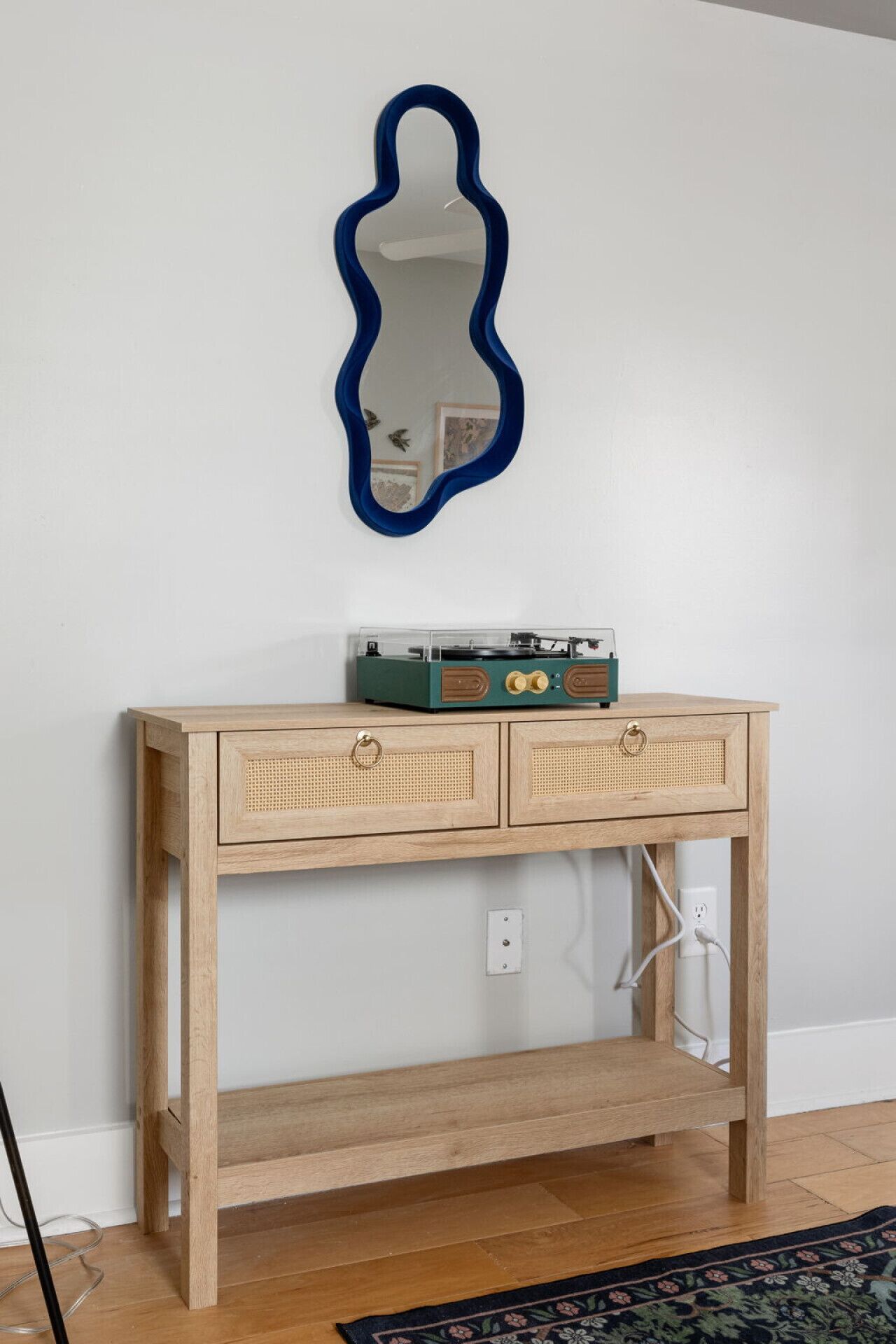A wooden console table with two drawers, a record player, and a blue mirror on the wall.