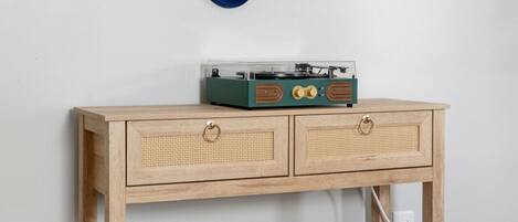 A wooden console table with two drawers, a record player, and a blue mirror on the wall.