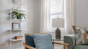 Un salón moderno con una silla de madera, un sofá verde, un estante blanco y una alfombra estampada.