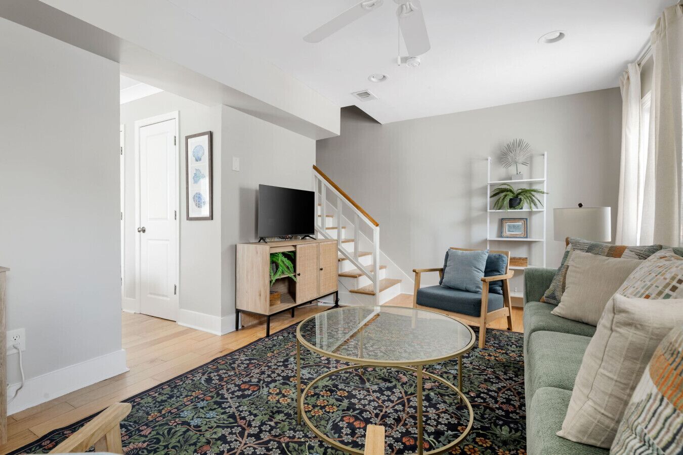 A modern living room with a glass coffee table, a green sofa, and a wooden cabinet with a TV.