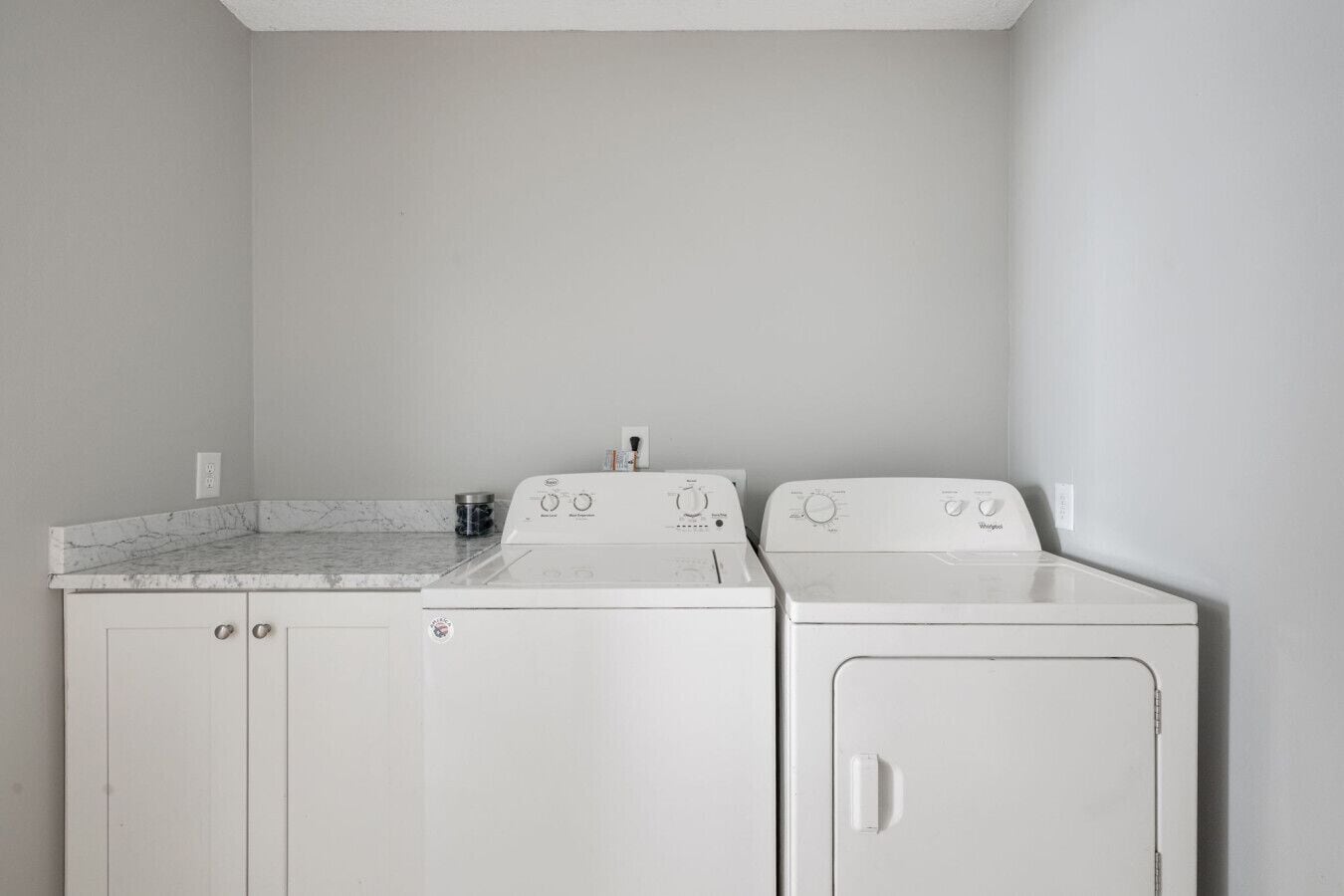 A laundry room with a washing machine and dryer, a marble countertop, and a white wall.