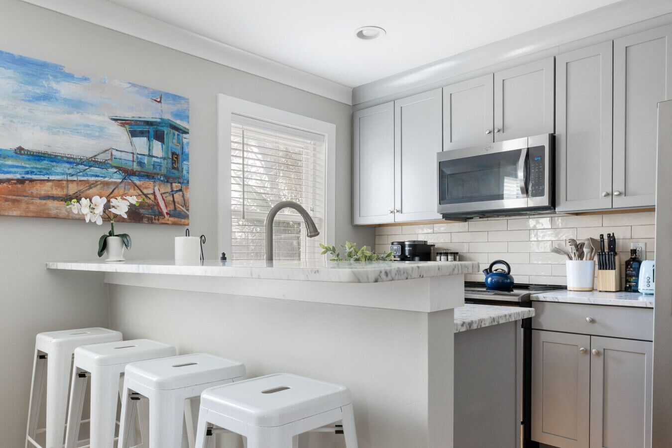 A modern kitchen with a marble countertop, stainless steel appliances, and a painting of a pier.