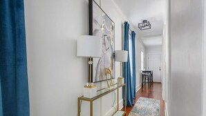 A hallway with a glass console table, two wall-mounted lamps, a large abstract painting, and a patterned rug. - Rutledge Ave - Renovated 2 Bed Home - Downtown! (Charleston)