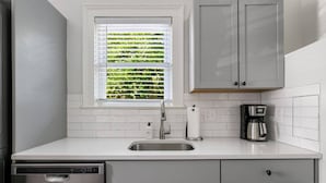 A kitchen with white cabinets, a stainless steel sink, a coffee maker, and a dishwasher. - Rutledge Ave - Renovated 2 Bed Home - Downtown! (Charleston)