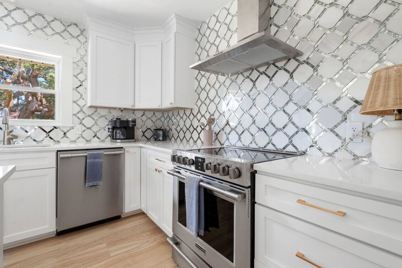 Una cocina moderna con armarios blancos, estufa de acero inoxidable y un salpicadero decorado.