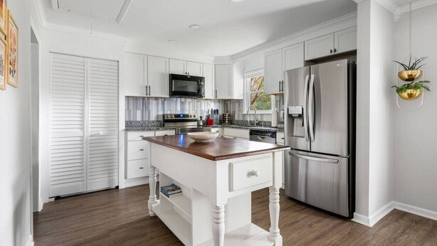 A modern kitchen with white cabinetry, stainless steel appliances, and a wooden island. - The Boroughs on Maxwell - 3 Bedroom (North Charleston)