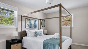 A four-poster bed with a white and teal bedspread, a nightstand with a lamp, and a wall-mounted artwork. - The Boroughs on Maxwell - 3 Bedroom (North Charleston)