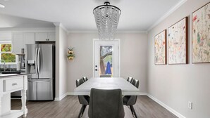 A modern kitchen with stainless steel appliances, a dining area with a large table and chairs, and a chandelier. - The Boroughs on Maxwell - 3 Bedroom (North Charleston)