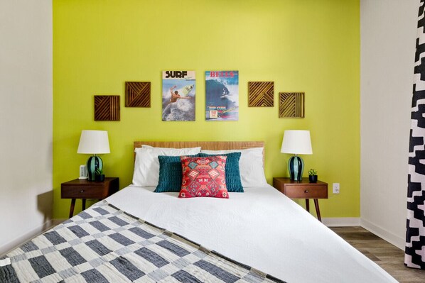 Una cama con colcha a cuadros, dos mesitas de noche con lámparas y una pared con carteles enmarcados.