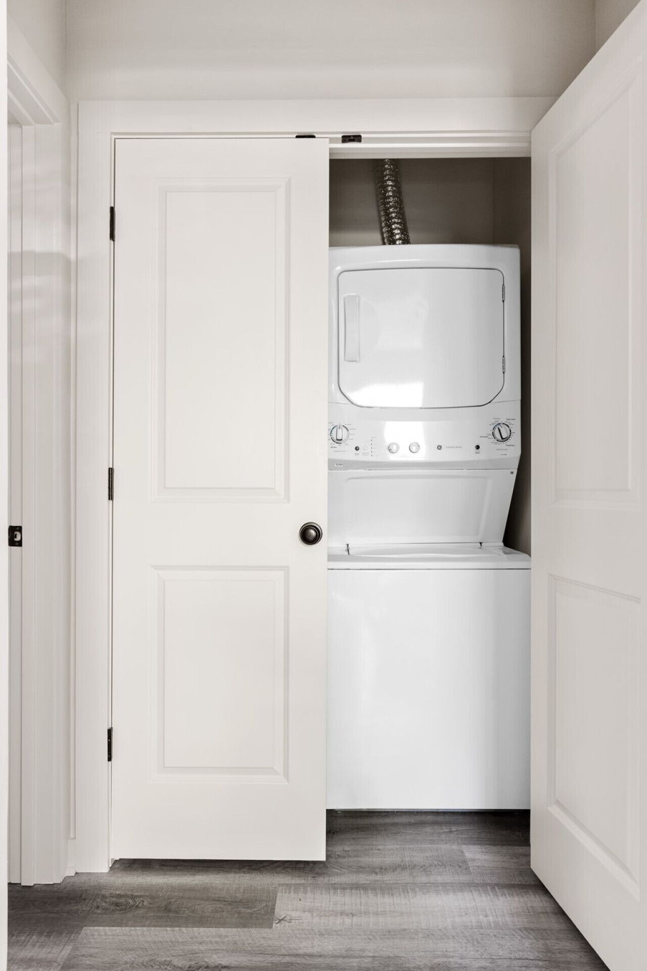 A laundry room with a white washing machine and dryer, a door with a black handle, and a wooden floor.