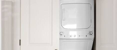 A laundry room with a white washing machine and dryer, a door with a black handle, and a wooden floor.