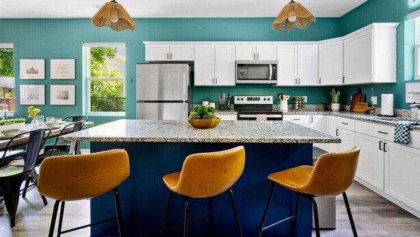 A modern kitchen with white cabinets, a central island with bar stools, and a large window providing natural light. - Stylish 3BR Near Downtown CHS (North Charleston)