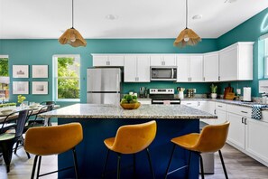 Una cocina moderna con armarios blancos, una isla central con taburetes y un amplio ventanal que proporciona luz natural.