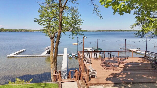 A wooden dock with tables and chairs, overlooking a calm lake with a boat docked nearby. - The Lake House at Darling Shores (Alexandria)