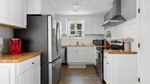 A modern kitchen with white cabinetry, stainless steel appliances, and a wooden countertop. - Folly Beach - 2 Blocks to Beach - Sleeps 6! (Folly Beach)
