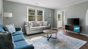 A living room with a grey sofa, blue armchair, and a coffee table. - Folly Beach - 2 Blocks to Beach - Sleeps 6! (Folly Beach)