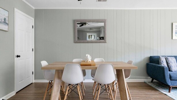 A dining area with a wooden table and four chairs, a mirror on the wall, a blue sofa, and a white door. - Folly Beach - 2 Blocks to Beach - Sleeps 6! (Folly Beach)