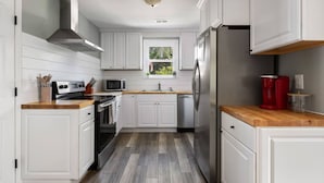 Cocina moderna con armarios blancos, campana extractora de acero inoxidable, microondas, lavaplatos y refrigerador.