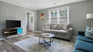 Una sala de estar con un sofá gris, un sillón azul, una mesita de centro y un televisor sobre un mueble de madera.