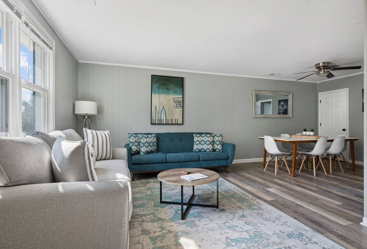 A living room with a sofa, a coffee table, a dining table with chairs, and a ceiling fan.