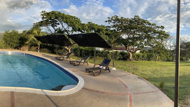 A swimming pool with lounge chairs and umbrellas, surrounded by greenery and a view of distant hills. - HOTEL CAMPESTRE LAS PALOMAS (Tocaima)