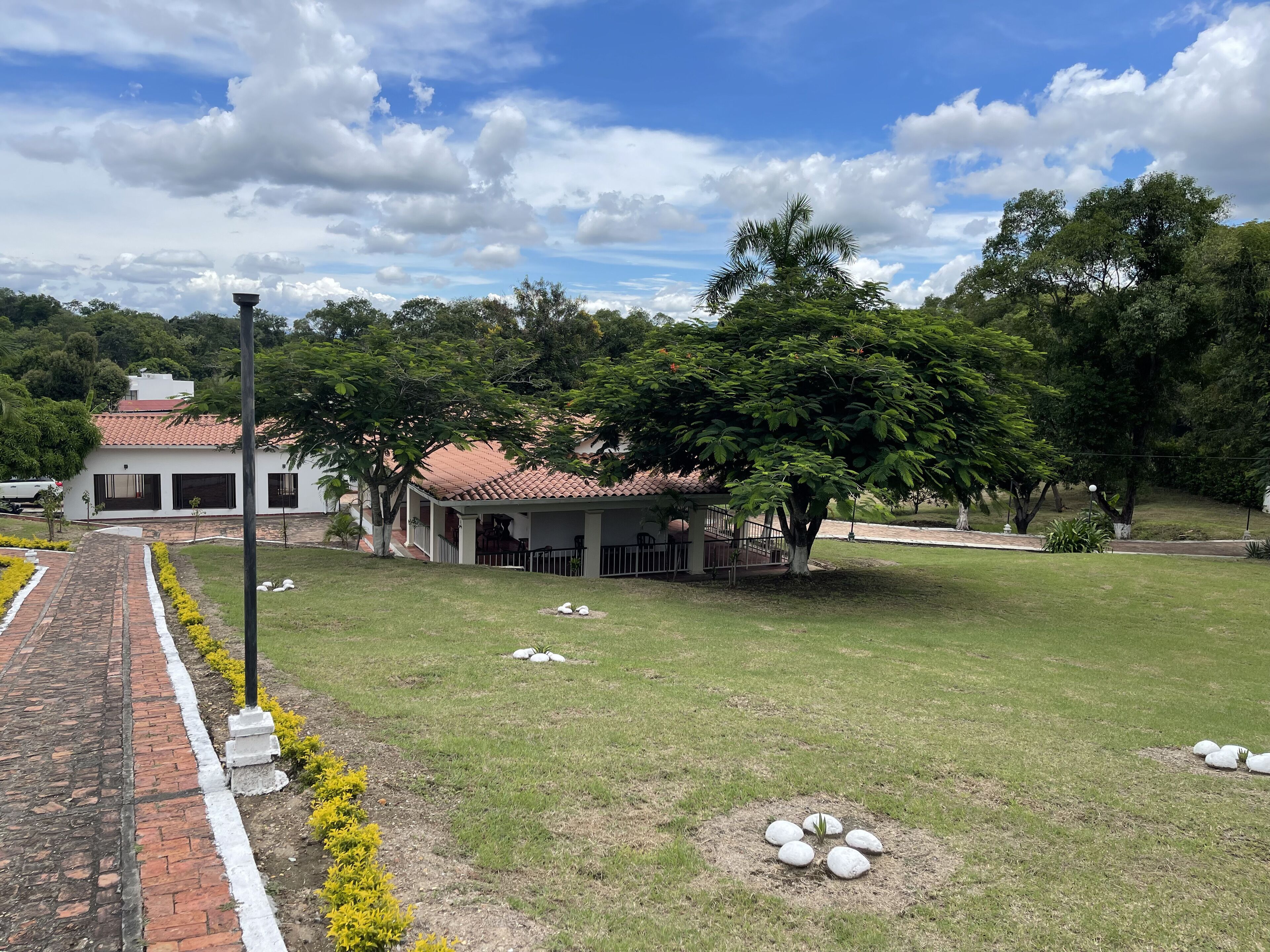 A white building with a red-tiled roof, surrounded by a grassy area with a paved walkway.