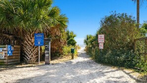 Un sendero arenoso que lleva a una playa con palmeras y un cartel que indica prohibido estacionar.