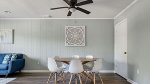 Un comedor con una mesa redonda y sillas blancas, un ventilador de techo y un adorno en la pared.