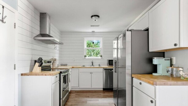 Una cocina moderna con armarios blancos, electrodomésticos de acero inoxidable y encimera de madera.